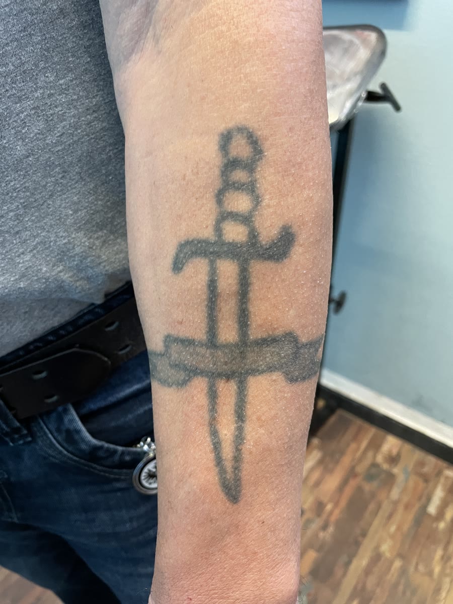 Verblasstes Dolch-Tattoo auf einem Unterarm vor dem Cover-up
