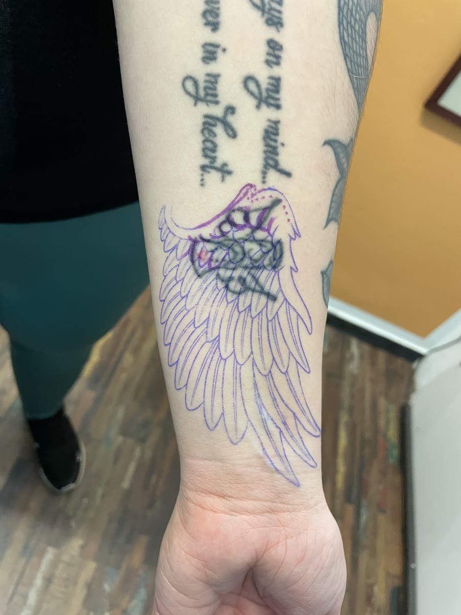 Flügel-Stencil über einem bestehenden Tattoo am Unterarm