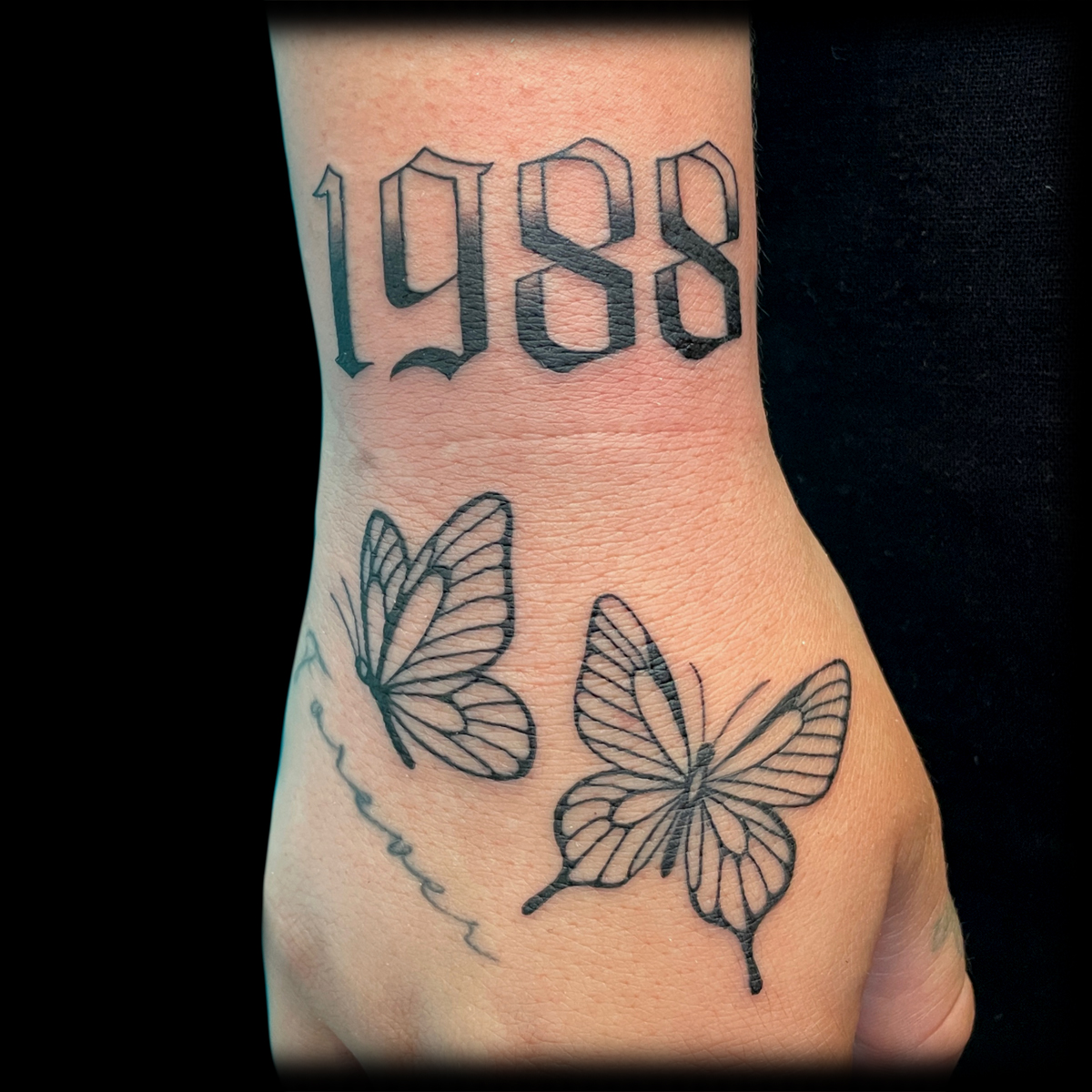 Feine Schmetterlinge und die Zahl 1988 als Tattoo auf einer Hand