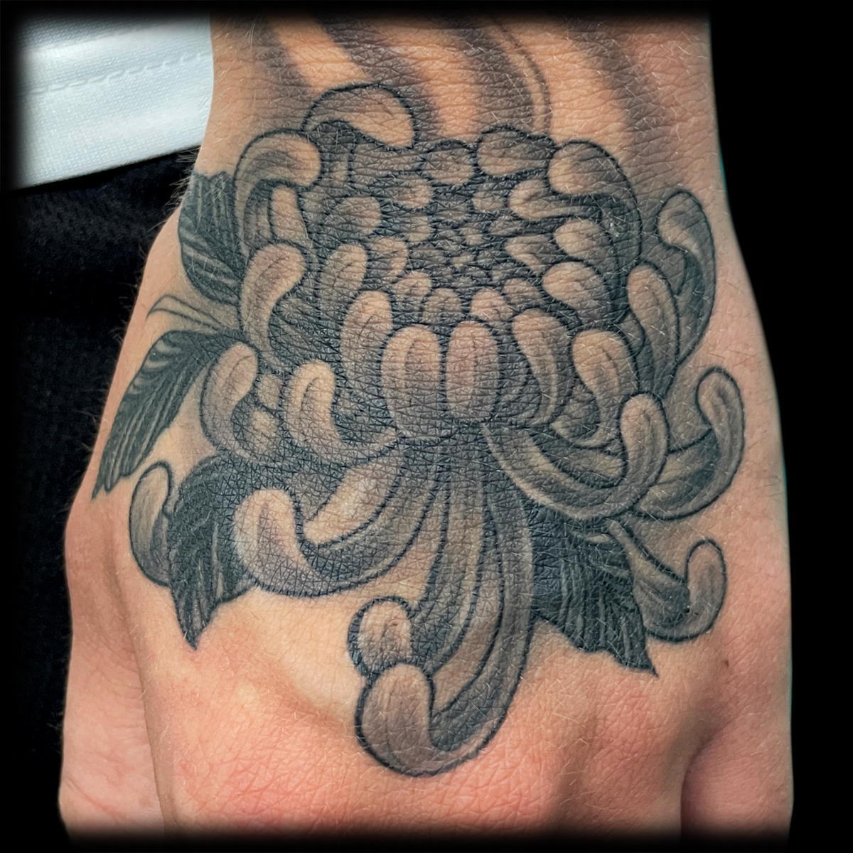 Schwarz-graues Chrysanthemen-Tattoo auf einer Hand