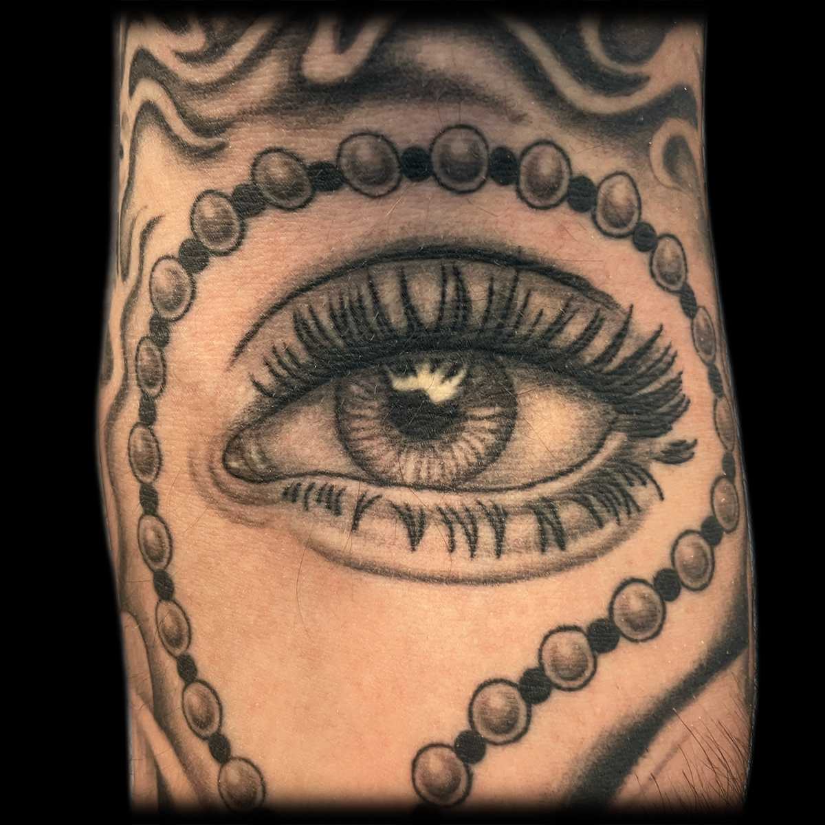 Schwarz-graues Augen-Tattoo mit Perlenmotiv in der Armbeuge