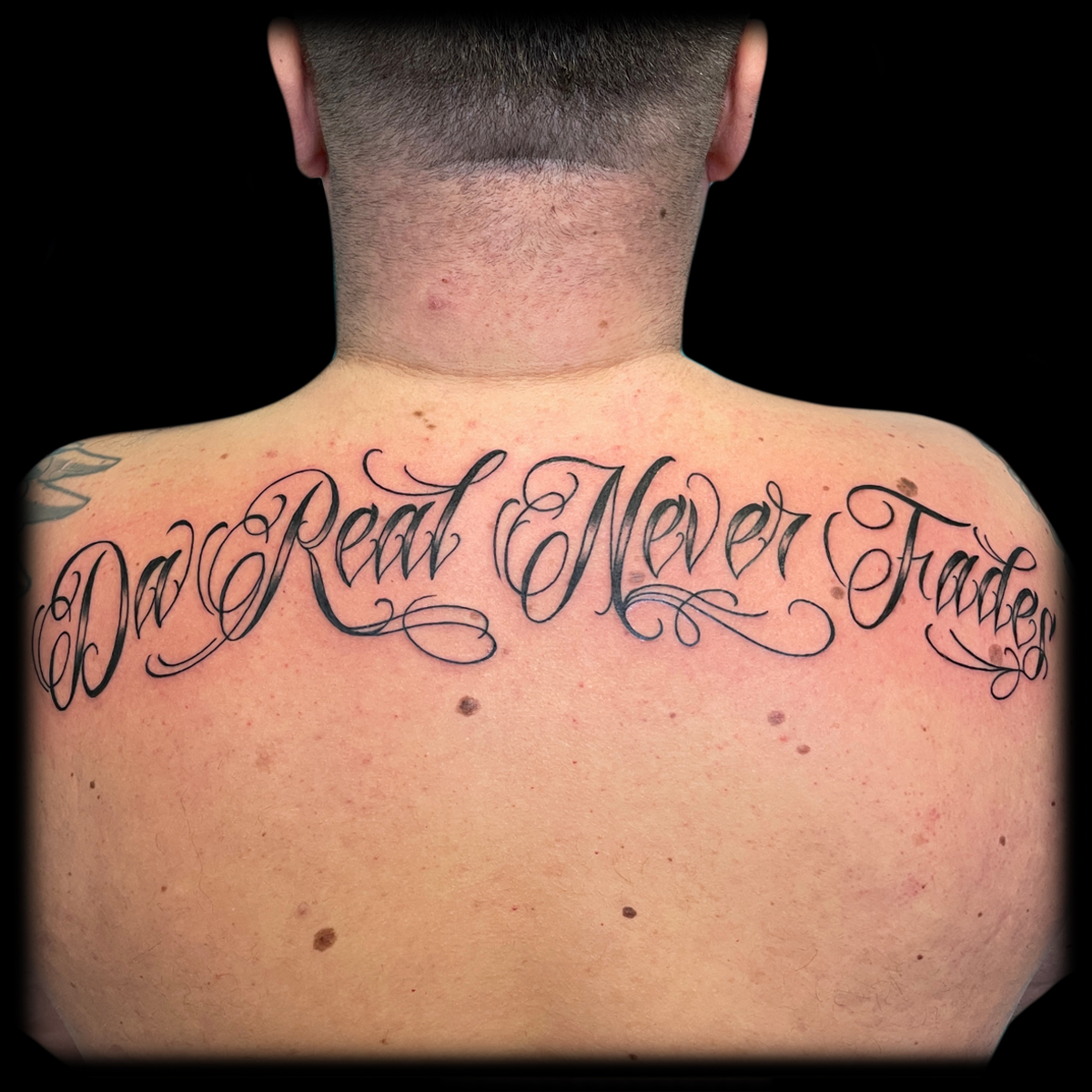 Großflächiges geschwungenes Lettering-Tattoo über dem oberen Rücken