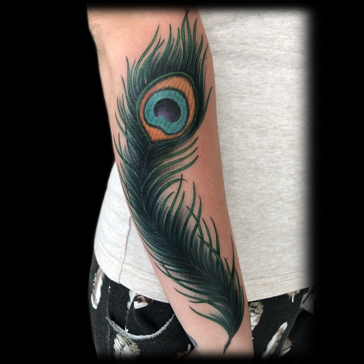 Farbiges Pfauenfeder-Tattoo auf einem Unterarm